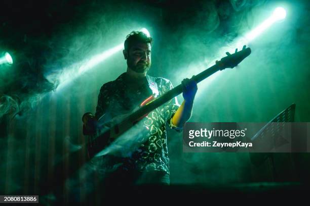 bass guitarist of the music band on stage with smoke and light effects - modern rock stock pictures, royalty-free photos & images