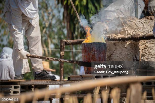 blacksmith holding a hot crucible by the iron pliers from furnace before pouring the melting gold into the statue block. - glowing hot steel stock pictures, royalty-free photos & images