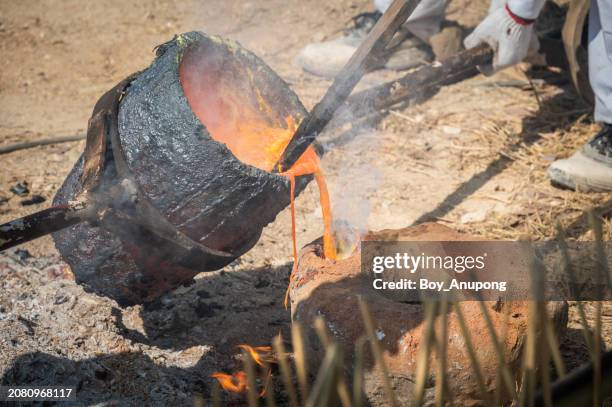 blacksmith holding a hot crucible by the iron pliers from furnace and pouring the melting gold into the statue block. - glowing hot steel stock pictures, royalty-free photos & images