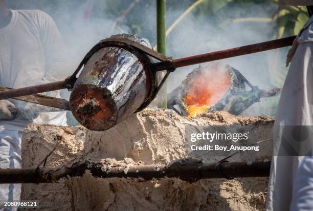 blacksmith holding a hot crucible by the iron pliers from furnace and pouring the melting gold into the statue block. - glowing hot steel stock pictures, royalty-free photos & images