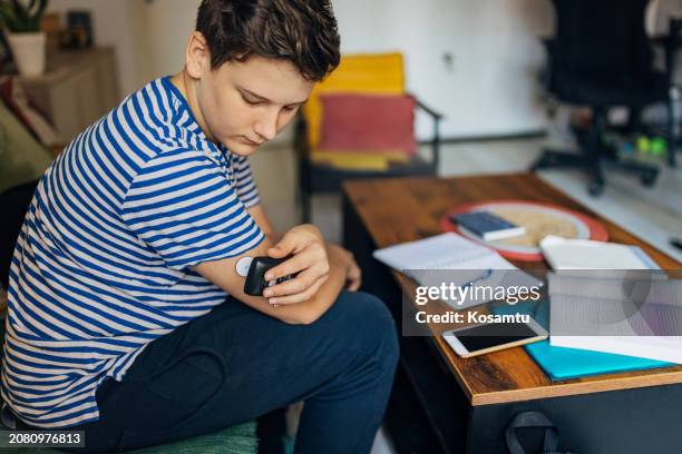 a teenage boy using a continuous remote glucose monitor diabetes sensor at home - glucose stockfoto's en -beelden