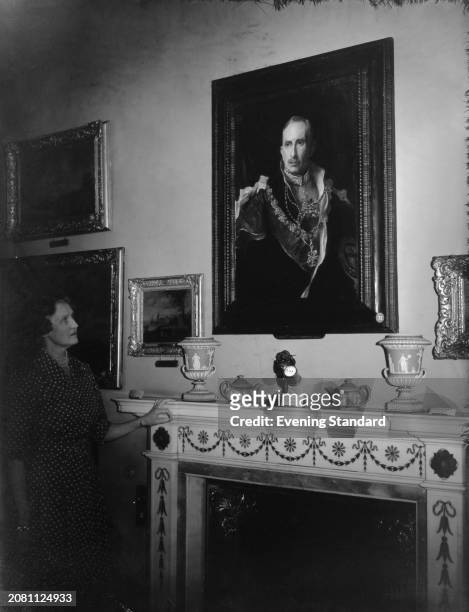 Helen Percy, Duchess of Northumberland looks at a painted portrait of her husband 'Alan Percy, 8th Duke of Northumberland' by Philip de László, above...
