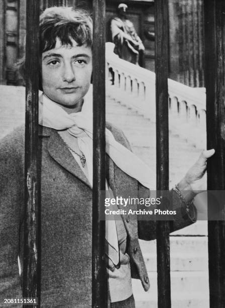 French novelist, playwright and screenwriter Francoise Sagan peers through the gate's iron bars outside the courthouse in Corbeil-Essonnes, a suburb...