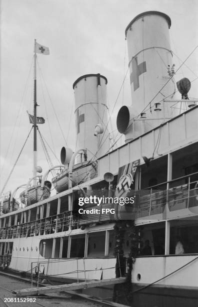 German Red Cross ship Ruegen, decorated with a banner featuring a swastika, with lifeboats along an upper deck, during a Second World War prisoner...