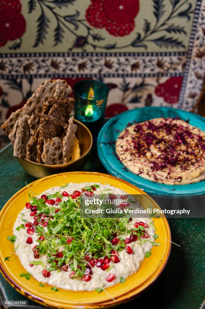Bowl of middle eastern hummus and aubergine spread with pomegranate seeds and micro herbs