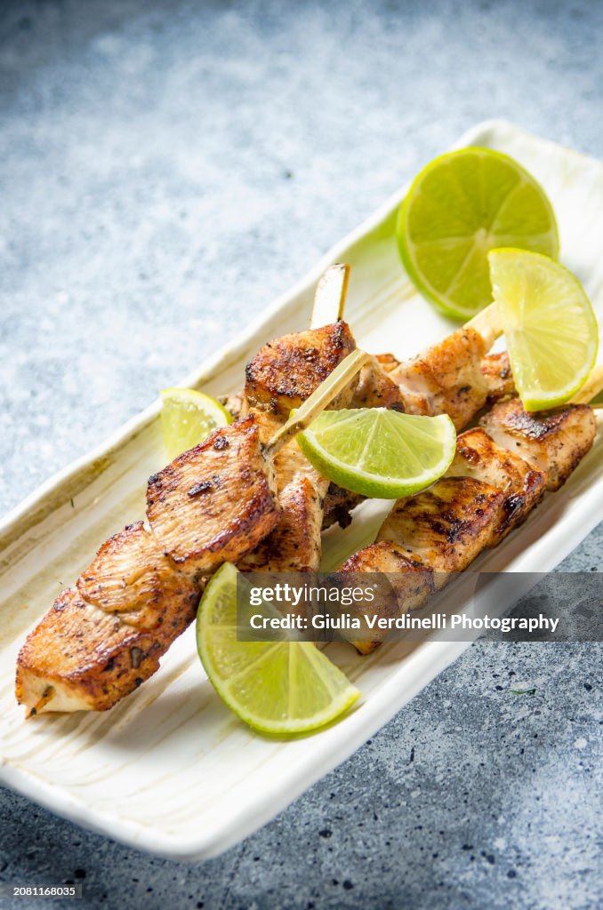 Grilled chicken breast skewers with lime on a light plate and light travertine marble table