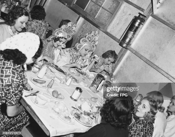 Dancers and performers, two still in costume, seated around a table as they take a break during filming for 'Rosalie' at Metro-Goldwyn-Mayer Studios...