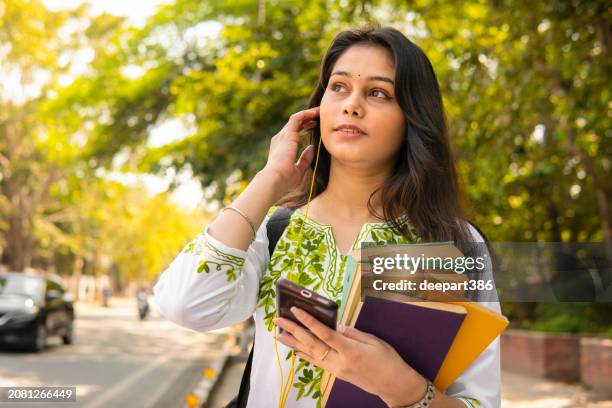 female college student with books walking on street and listening music with earphones. - kurta stock pictures, royalty-free photos & images