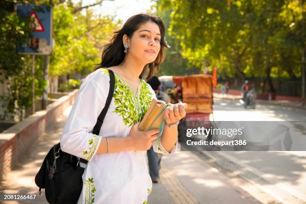 female college student with books and backpack waiting for a bus or taxi. - kurta stock pictures, royalty-free photos & images