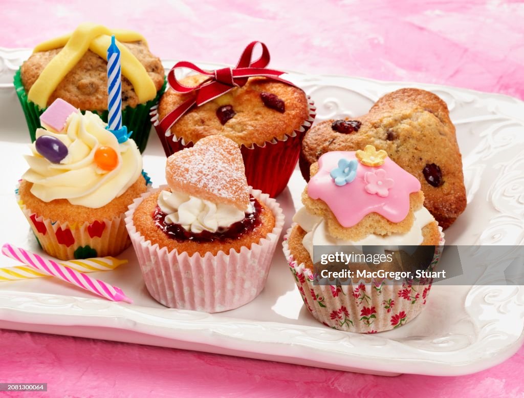 A selection of different celebration cupcakes on a cream plate and pink background