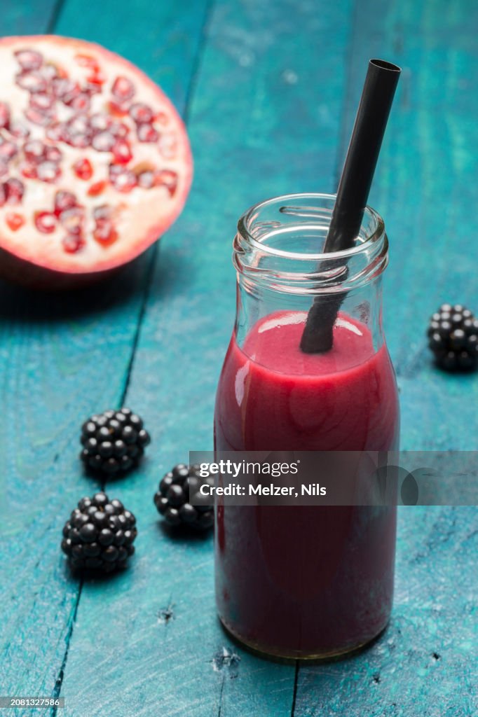 A blackberry and pomegranate smoothie in a bottle with a straw