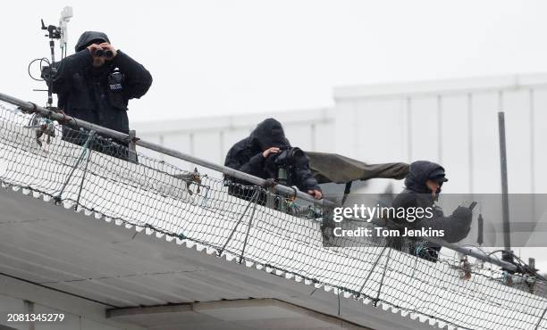 Police spotters with a gun wrapped up looking over the course from the roof of one of the main stands during racing on day two of the Grand National...