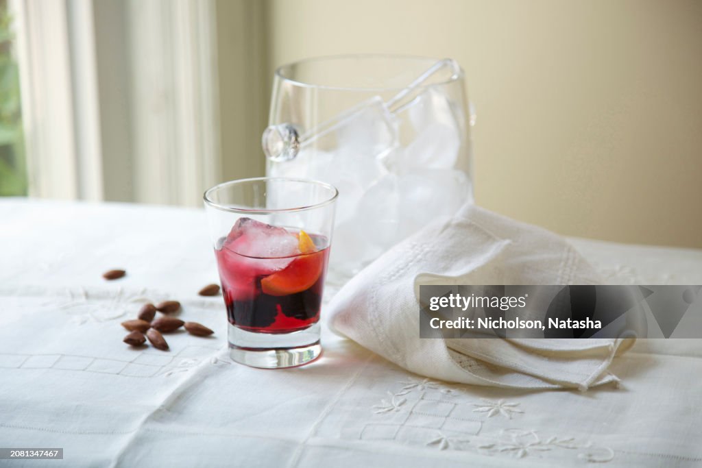 Cocktail With Ice Bucket, Almonds and Cloth Napkin On Table Beside Window