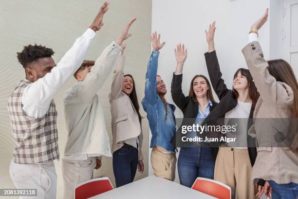 diverse team of colleagues celebrating success with raised arms in a bright office environment - corporate modern office bright diverse imagens e fotografias de stock