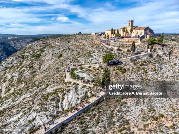 aerial view, mountain pedestrian path with curves on a mountain leading to a hermitage with people walking in traditional festival clothes. - bernat bacete stock pictures, royalty-free photos & images