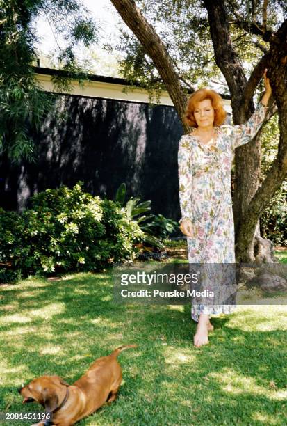 Actress Rita Hayworth, wearing a Diane von Furstenberg floral print dress, poses for portraits while playing with her dachshund during an interview...
