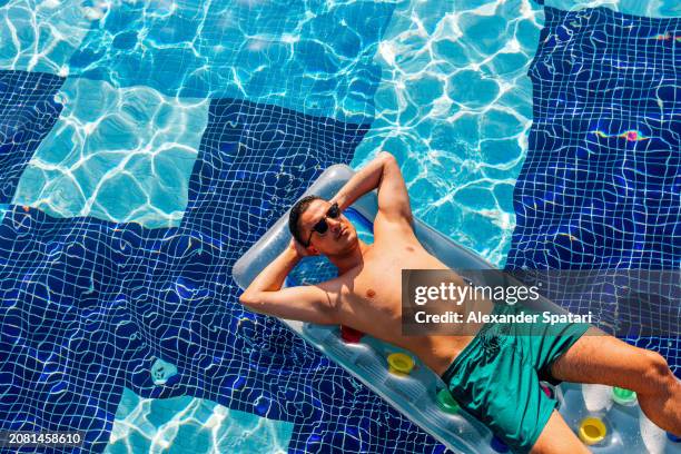 man in sunglasses relaxing on inflatable raft in the swimming pool on a hot sunny summer day, high angle view - floating on water stock pictures, royalty-free photos & images