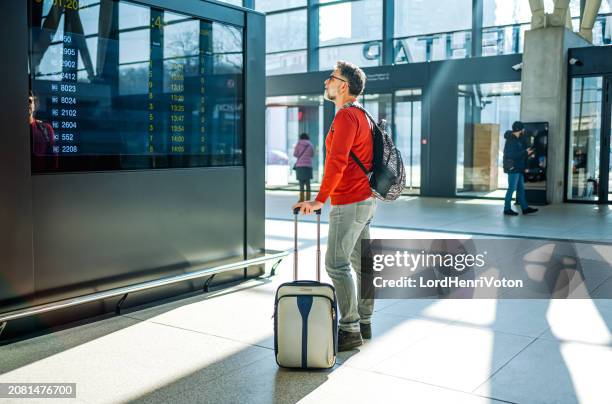 pasajero mirando el tablero de horarios en una estación de ferrocarril - equipaje de mano fotografías e imágenes de stock