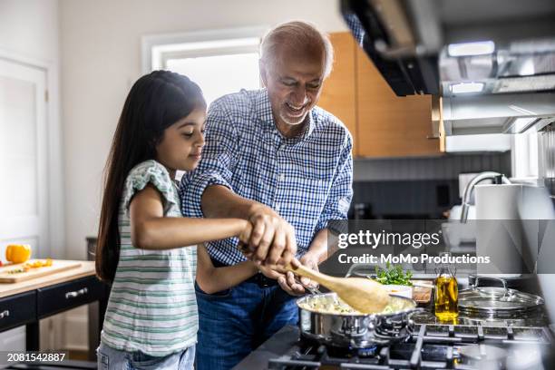 grandfather and granddaughter cooking in kitchen - roer stockfoto's en -beelden