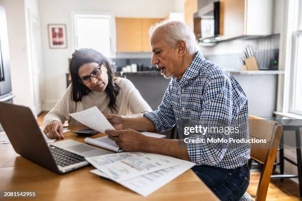 senior couple paying bills at kitchen table - debiteuren stockfoto's en -beelden