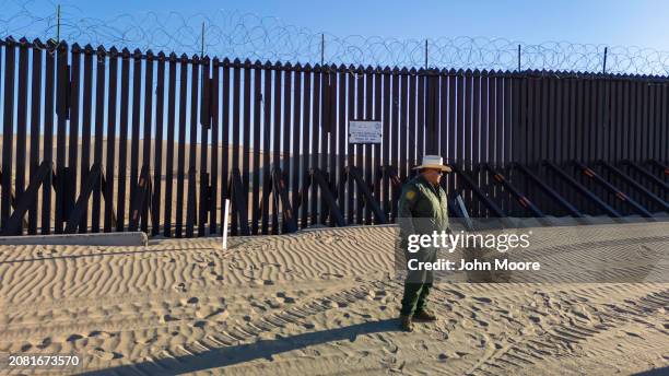 Border Patrol agent stands near the border fence which stretches through the Imperial Sand Dunes on March 8, 2024 in Imperial County, California. The...