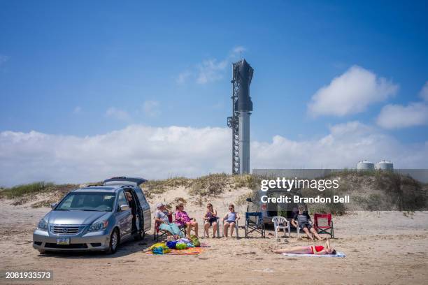 People spend time on the beach near the Starship Flight 3 Rocket a day before its scheduled launch at the Starbase facility near Boca Chica beach on...