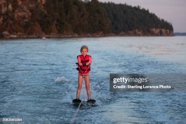 a young girl having fun learning to water ski behind a boat with a pair of beginner water skis, with adult supervision and a life jacket on in the gulf islands, near gabriola and salt spring island on a summer sunny day in the pacific ocean - gabriola isle stockfoto's en -beelden