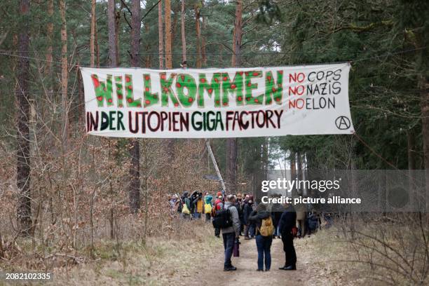 March 2024, Brandenburg, Grünheide: People gather for a walk under a banner with the words "Welcome to the Utopia Giga Factory No Cops No Nazis No...