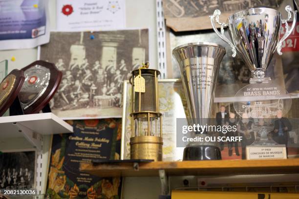 An inscribed miner's lamp is displayed next to awards, certificates and historic photographs of the Carlton Main Frickley Colliery Band in their band...