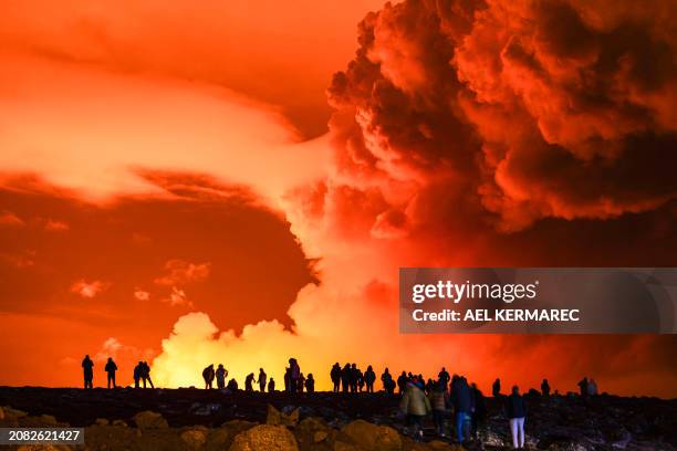 People gather to watch as molten lava flows out from a fissure on the Reykjanes peninsula north of the evacuated town of Grindavik, western Iceland...