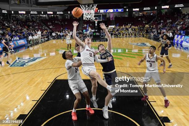 Aanen Moody and Dischon Thomas of the Montana Grizzlies fight Brian Goracke of the Montana State Bobcats for a rebound in the first half during the...