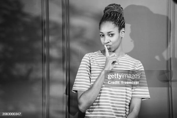 young woman with finger on lips against gray wall - black and white instant print stock pictures, royalty-free photos & images