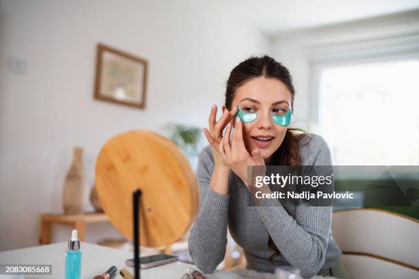 hermosa mujer joven que aplica parches de recuperación de hidrogel debajo de los ojos en casa - debajo de fotografías e imágenes de stock