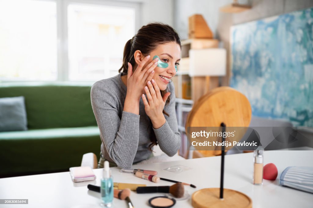 Beautiful young woman applying hydrogel under-eye recovery patches at home