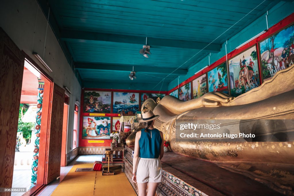 Young woman with hat visiting a lying Buddha in Chang Mai
