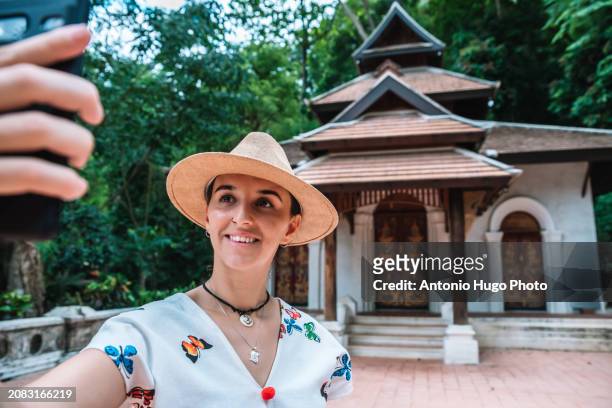 young smiling woman taking a selfie at wat phra lat mountain temple in chang mai - art of the vintage selfie stockfoto's en -beelden