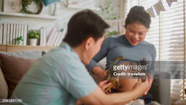 sweet asian happiness new parent couple asia cheerful pregnant woman getting ready for her new born bab funny humor playing dinosaur toy on wife belly laught joyful moment at home - laught imagens e fotografias de stock