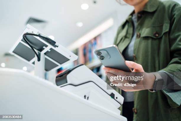 close up of a woman's hand making mobile payment with her smartphone in a shop, scan and pay a bill on a card machine making a quick and easy contactless payment at self checkout counter. nfc technology, tap and go concept - brand name mobile payment photos et images de collection