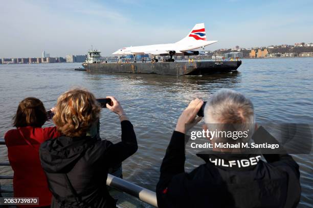 People watch as retired British Airways Concorde supersonic airliner is moved by a barge on the Hudson River on March 14, 2024 in New York City. The...