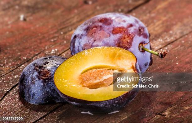 whole and halved plums on a wooden surface - wooden surface finishes foto e immagini stock
