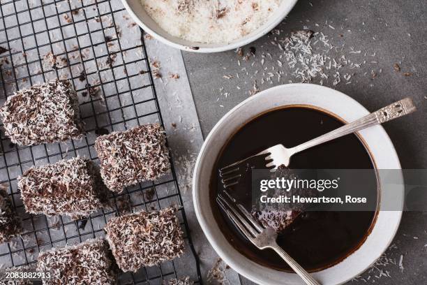 making lamingtons - dipping in chocolate icing - lamington cake stock pictures, royalty-free photos & images