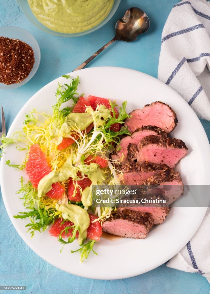 Healthy pork dinner with grapefruit and frisee on white plate