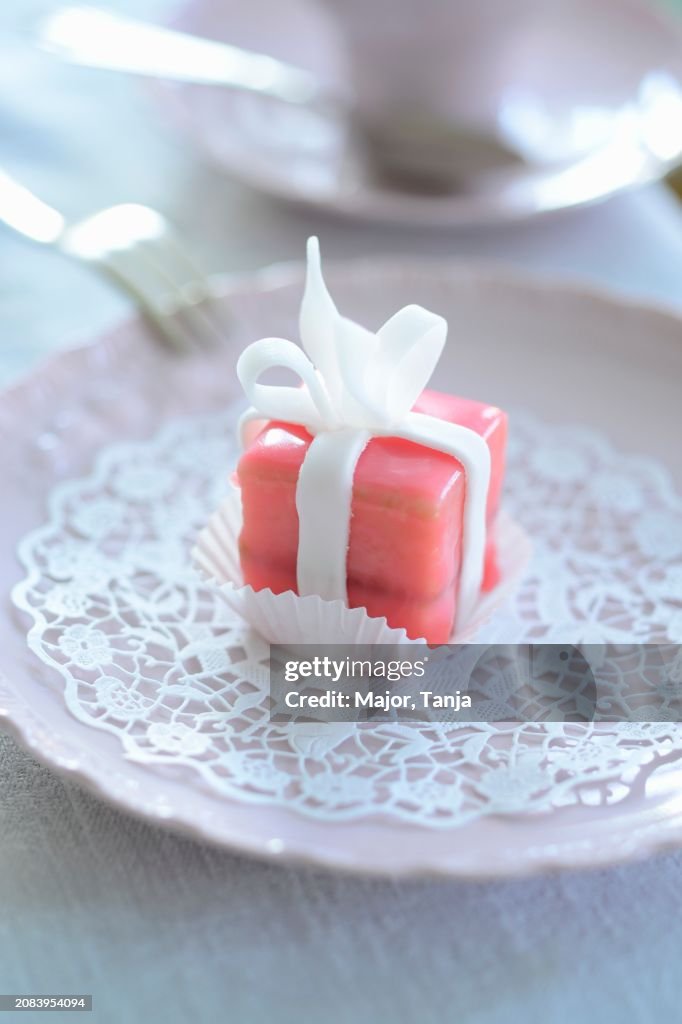 A pink petit four on a paper doily
