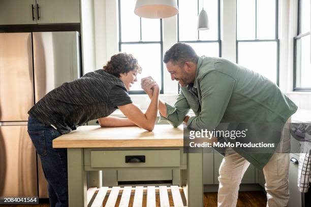father and teen son arm wrestling in kitchen - momo challenge stockfoto's en -beelden