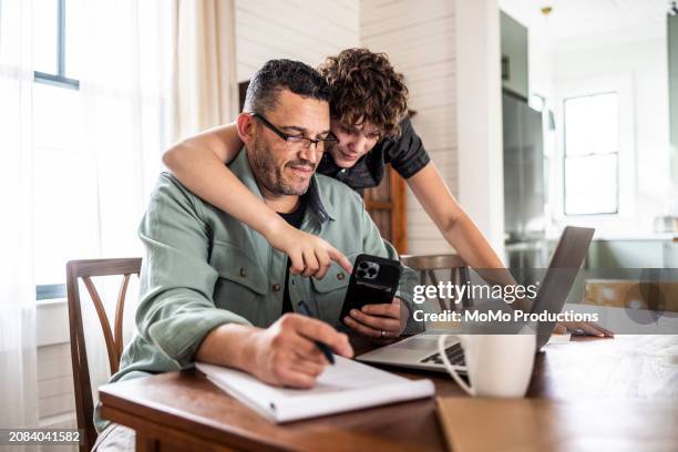 father working from home with teenage son - family with phone photos et images de collection