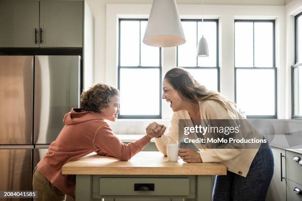 mother and preteen son arm wrestling in kitchen - momo challenge stock pictures, royalty-free photos & images