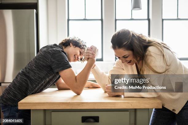 mother and teenage son arm wrestling in kitchen - momo challenge stockfoto's en -beelden