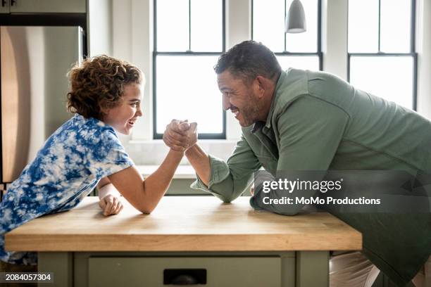 father and preteen son arm wrestling in kitchen - momo challenge stockfoto's en -beelden