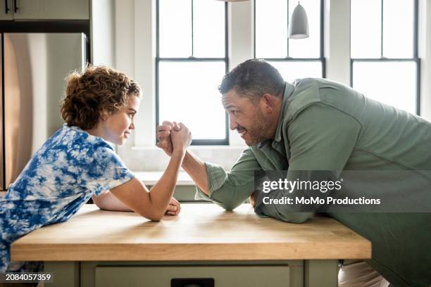 father and preteen son arm wrestling in kitchen - momo challenge stockfoto's en -beelden