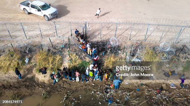 In an aerial view, immigrants pass through coils of razor wire while crossing the U.S.-Mexico border on March 13, 2024 in El Paso, Texas. The wire...